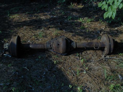1988 Ford Bronco - A rusty rear axle assembly rests on the forest floor, awaiting restoration.