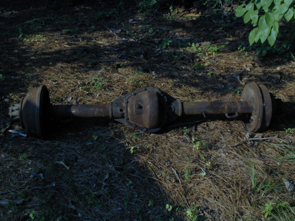 Rusty rear axle assembly with brake drums, lying on the ground