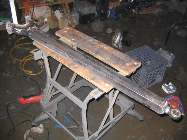 Two long steel beams on plywood across a folding work stand on a garage floor with extension cords
