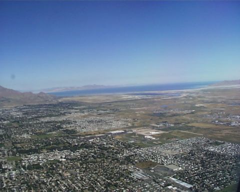 1988 Ford C-350 (Centurion Conversions) - An expansive aerial perspective captures a urban landscape adjacent to a vast body of water, with distant mountains under a clear sky.