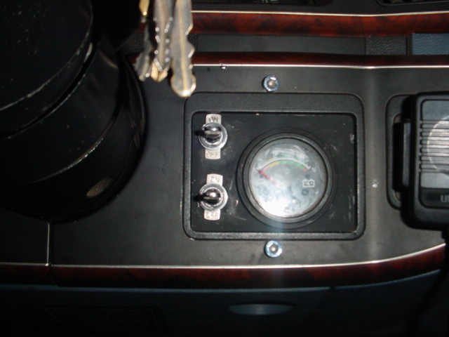 Center console gauge panel with two toggle switches and a small round meter, woodgrain trim, keys hanging