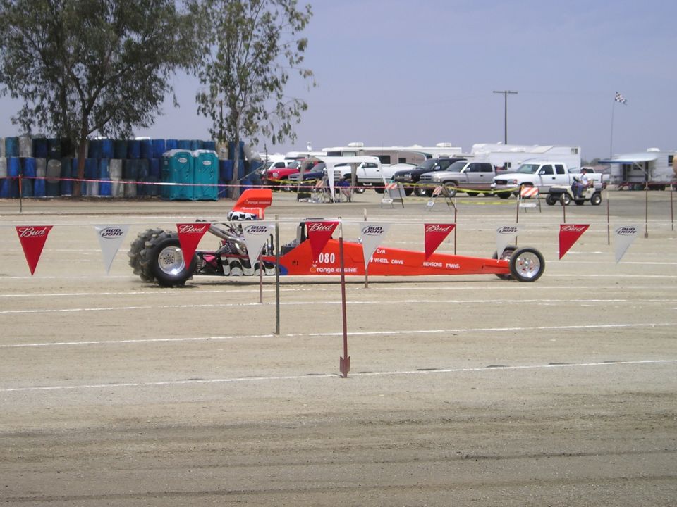 Orange dragster with large rear tires and Bud Light flags on poles. Text on side reads .080 GEORGE & ANNE