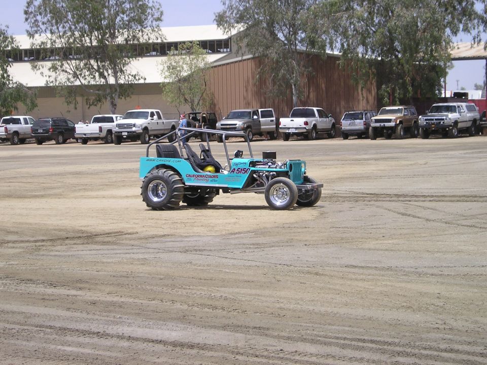Teal tube-chassis sand drag buggy with exposed V8 on a dirt track