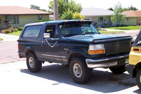 1995 Ford Bronco - Dark green full-size Ford Bronco with a matching removable hardtop and a chrome billet-style grille, mildly lifted on chrome wheels, parked…