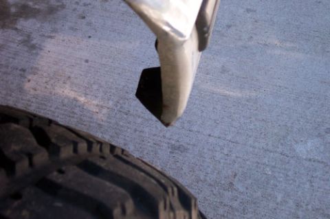 1995 Ford Bronco - Low-angle detail of a white body panel's lower front corner and mud flap edge above a concrete driveway, with the aggressive lugged tread o…