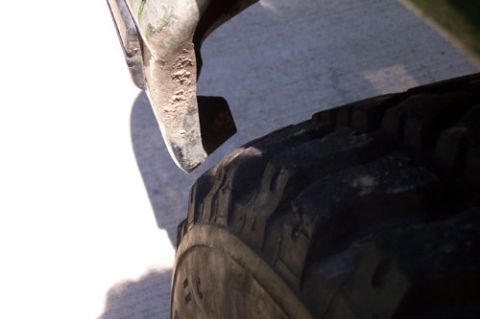 1995 Ford Bronco - Close-up looking down at the chunky lugs of a mud-terrain off-road tire beside the scuffed lower edge of a body panel, on a sunlit concrete…