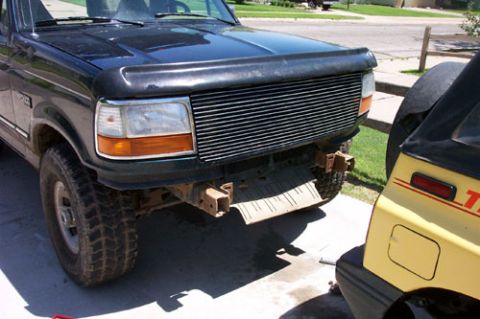 1995 Ford Bronco - Front three-quarter view of a dark green 1990s full-size Ford truck/Bronco on a concrete driveway, fitted with a billet-style horizontal-ba…