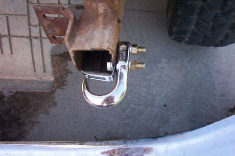 1995 Ford Bronco - A chrome tow/recovery hook bolted into a square receiver-hitch mount at the rear of a vehicle, above a rusty bracket, with an off-road tire…