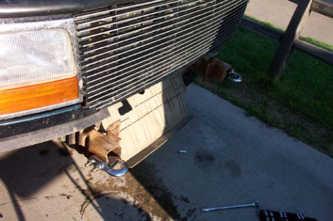 1995 Ford Bronco - Low-angle shot of the front end of a 1990s Ford truck with the bumper removed, exposing the rusty frame horns and two blue-painted tow hook…