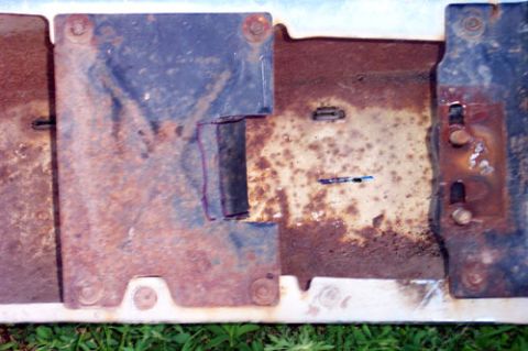 1995 Ford Bronco - Overhead close-up of a heavily rusted steel bracket assembly, with two thick reinforcement plates bolted to a flat mounting panel and marke…