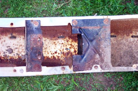 1995 Ford Bronco - Backside of a removed front bumper laid face-down in the grass, showing heavy surface rust across the pressed-steel channel and the two bol…