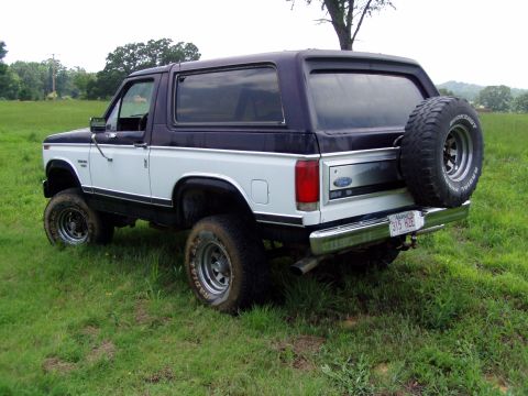 1983 Ford Bronco - This two-tone Ford Bronco is viewed from its rear three-quarter angle, sitting in a field.