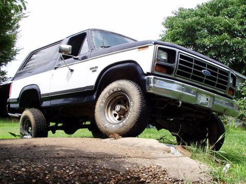 1983 Ford Bronco - Low-angle driver's-side front three-quarter view of a white and dark blue two-tone full-size Ford Bronco parked on grass beside a concrete…