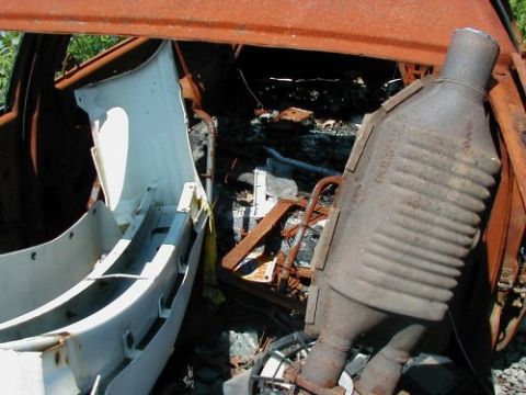 1997 Ford Taurus - The interior of a vehicle shows extensive fire damage, with a catalytic converter and part of the bumper still attached.