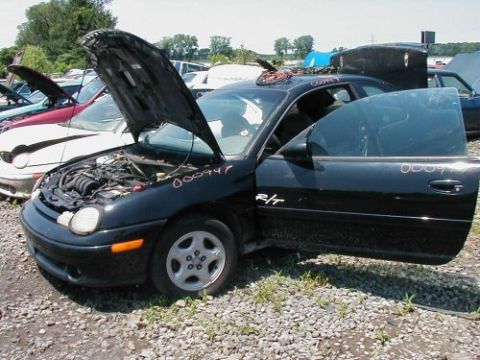 1997 Ford Taurus - A black Dodge Neon R/T sits in a junkyard with its hood and driver's door open, revealing its engine and interior.