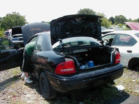 1997 Ford Taurus - Junkyard scene with a black sedan, trunk open, and a person reaching inside. Other cars are visible in the background.