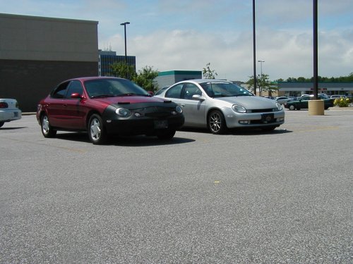 1997 Ford Taurus with a car bra, parked next to a silver Dodge Neon in a parking lot