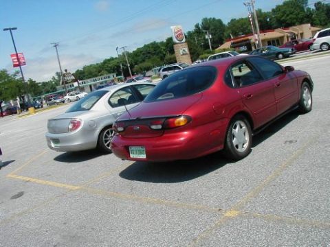 1997 Ford Taurus - A red 1997 Ford Taurus is seen from the rear in a parking lot next to a silver sedan.