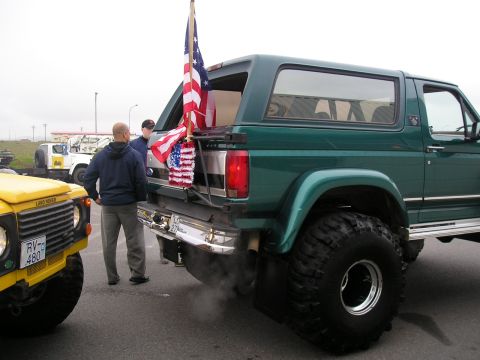1996 Ford Bronco - A green Ford Bronco is parked next to a yellow Land Rover, with an American flag displayed on the back of the Bronco.
