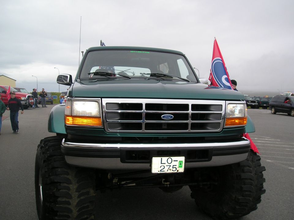 Front of lifted green Ford on large mud tires with LO-275 plate and red flag