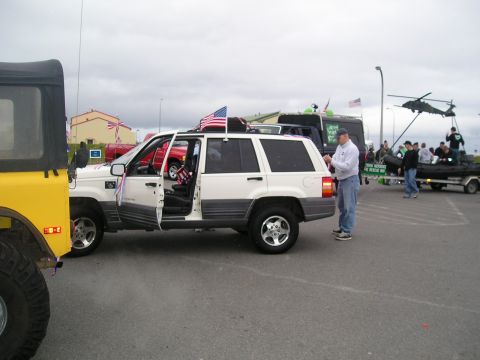 1996 Ford Bronco - A white Jeep Grand Cherokee is parked with its doors open, adorned with American flags, as part of an outdoor event.