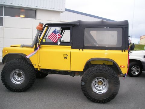 1996 Ford Bronco - Yellow off-road vehicle with snorkel and American flags parked next to another vehicle.