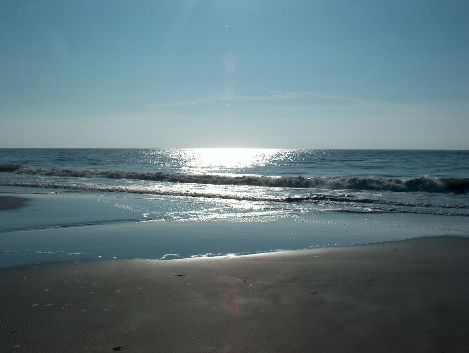 Ocean waves on a sandy beach with the sun reflecting on the water