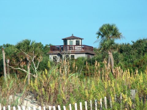1998 Ford Taurus - A beach house with a balcony is seen through palm trees and tall grass.