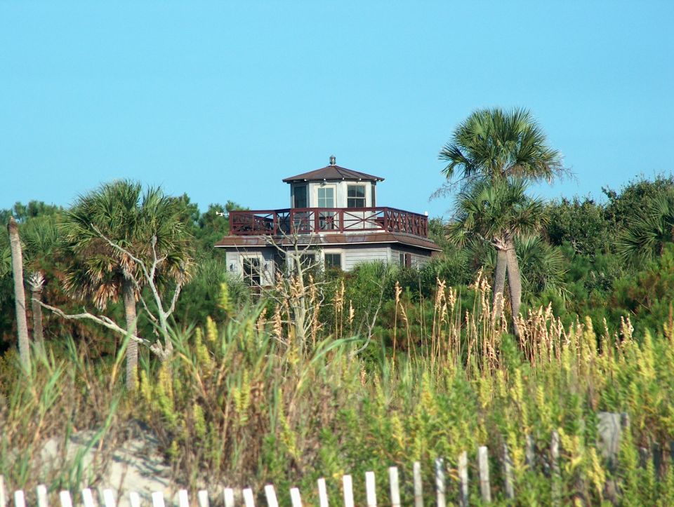 Beach house with a balcony surrounded by palm trees and tall grass
