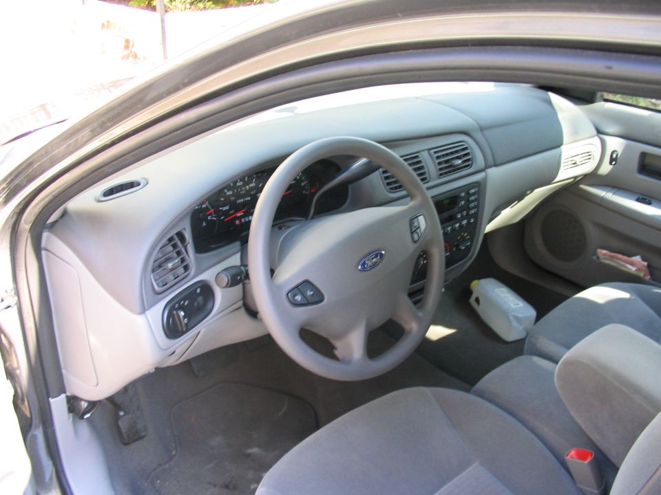 Gray Ford sedan interior showing steering wheel, gauge cluster and cloth seats through open door