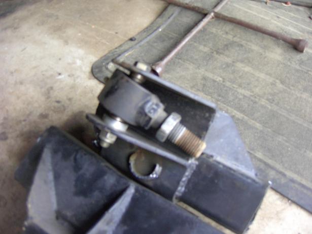 Close-up of a black steel suspension bracket with a large threaded bolt and nut on a concrete floor.