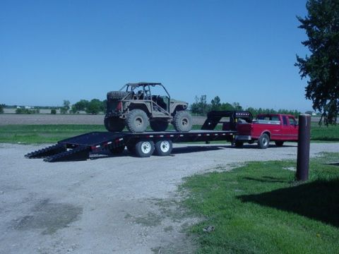 1992 Ford Bronco - A red pickup truck is hauling a flatbed trailer carrying a tan off-road buggy under a clear blue sky.