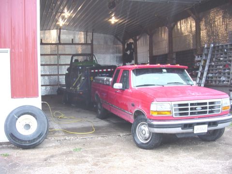1992 Ford Bronco - A red Ford F-Series truck from 1995 is parked in a barn, towing a trailer with a green utility vehicle.