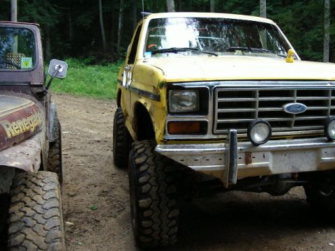 1985 Ford Bronco - A yellow Ford Bronco is parked next to a brown Jeep Renegade on a dirt road.