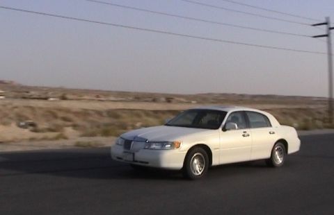 2002 Lincoln Town Car - A white 2002 Lincoln Town Car is seen driving on a road with a desert landscape under a clear sky.
