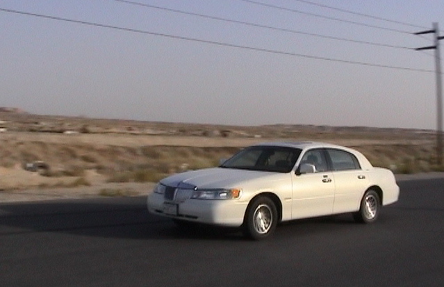 White Lincoln Town Car sedan on a desert road, 3/4 front view with power lines behind