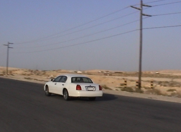 White Lincoln Town Car parked on a desert roadside, seen from the rear three-quarter