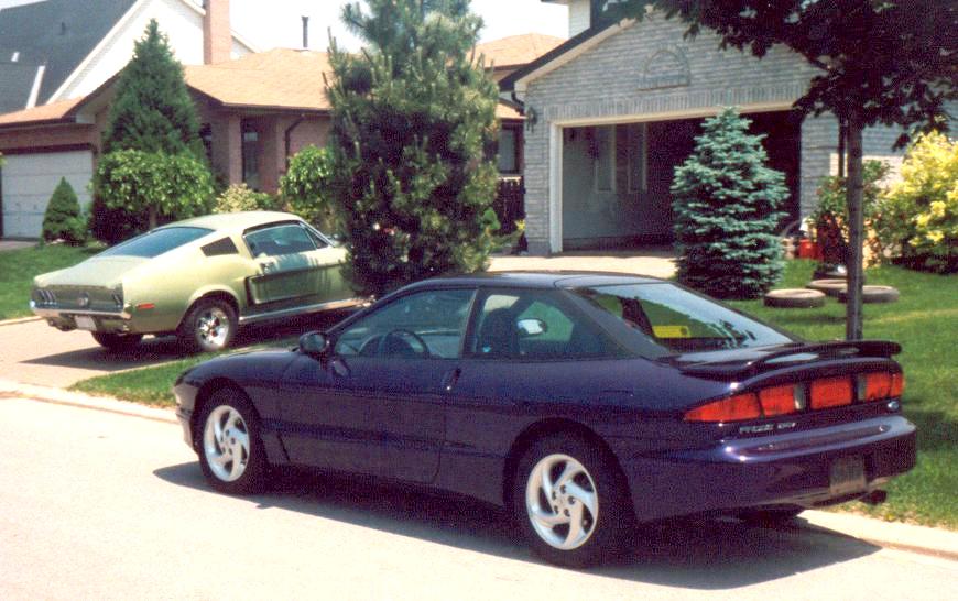 Dark blue Ford Probe coupe in driveway with a green Mustang fastback parked behind it