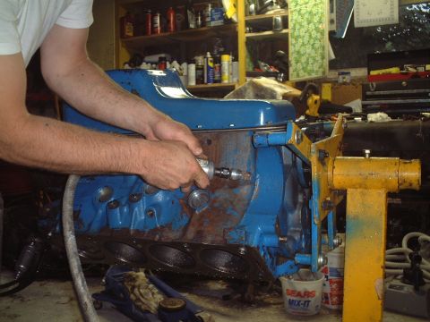 1967 Ford Galaxie - Working on an engine block in a garage setting. Tools and shelves are visible in the background.