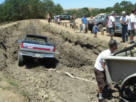 1989 Ford Bronco - A Ford pickup truck is stuck in a deep mud trench while onlookers watch from the embankment.