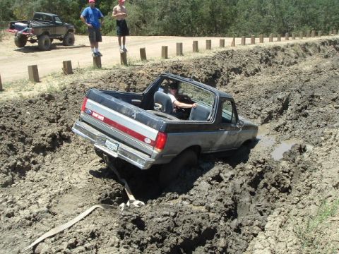 1989 Ford Bronco - A Ford Bronco navigates a muddy obstacle course with onlookers.