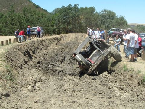 1989 Ford Bronco - Spectators watch as an off-road vehicle gets stuck in a mud pit during an event.