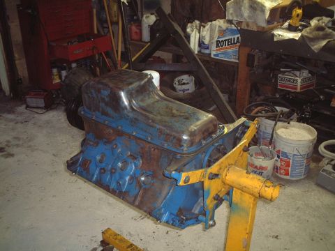 1967 Ford Galaxie - An engine block, painted blue and showing signs of rust, sits on a yellow engine stand in a cluttered garage.