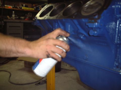 1967 Ford Galaxie - Someone is painting an engine block blue with a spray can in a workshop.