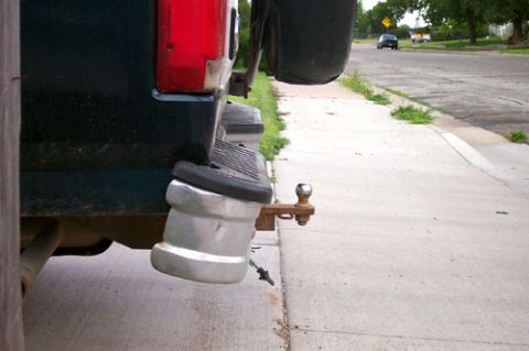 1995 Ford Bronco - Low rear-corner view of a dark green truck at a curb showing a badly mangled chrome rear step bumper, crushed and folded down and away from…