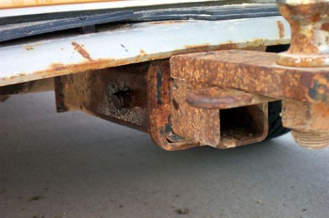1995 Ford Bronco - Close-up from below of a heavily rusted rear bumper and receiver-hitch assembly on a truck, with a square hitch tube, corroded mounting bra…