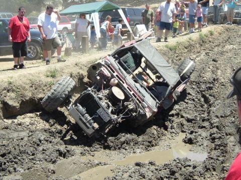 1989 Ford Bronco - An off-road vehicle is stuck in a muddy ditch, with onlookers gathered around.