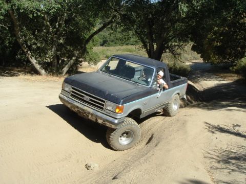 1989 Ford Bronco - A two-tone Ford F-Series truck navigates a dirt trail with its front wheels at an angle.