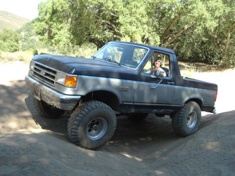 1989 Ford Bronco - Ford Bronco navigates a dirt trail with a driver behind the wheel.