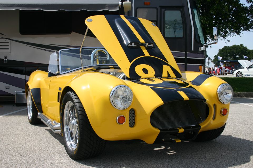 Yellow Cobra-style roadster with black stripes, number 84, hood up, chrome side pipes